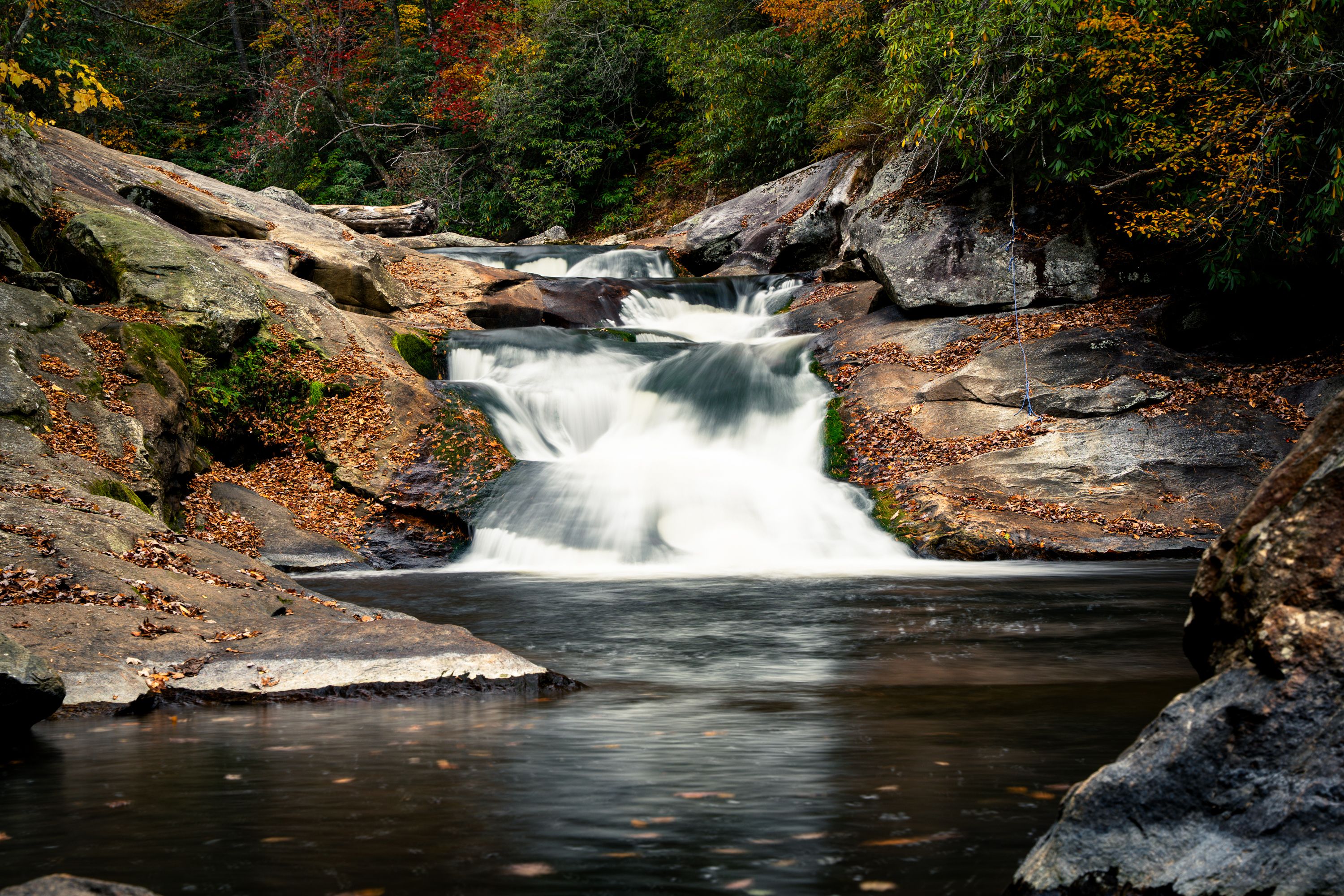 Long-exposure autumn creek cascading over broad rock ledges